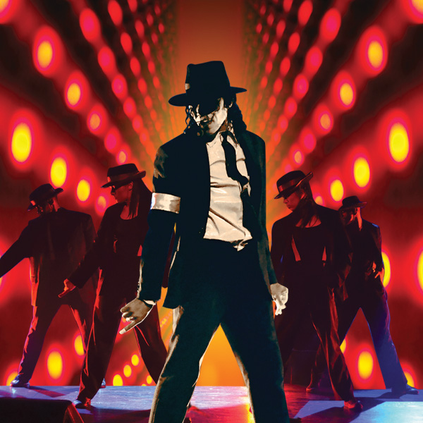 A performer in a black suit, white shirt, hat, and white armband poses dramatically on stage, flanked by four similarly dressed dancers, against a vibrant red and orange background with glowing circular lights.