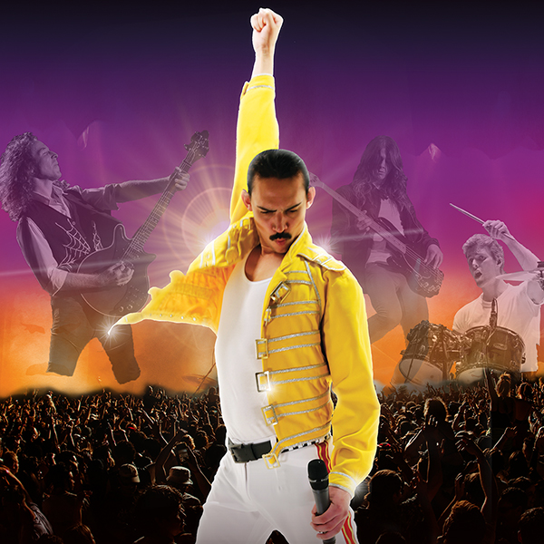 A performer dressed as Freddie Mercury poses on stage with one fist raised. Behind him, band members play guitar and drums. The crowd cheers in front of a vibrant purple and orange background.